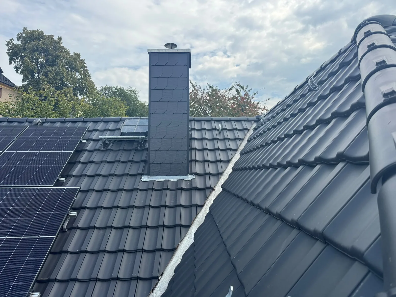Dunkles Ziegeldach mit Photovoltaikmodulen und verkleidetem Schornstein